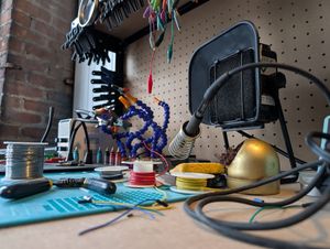 A photo of a soldering bench, with the focus on the soldering iron in the background, with wires in the foreground