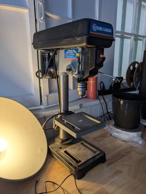 A photo of a drill press, dramatically-lit next to a broad light